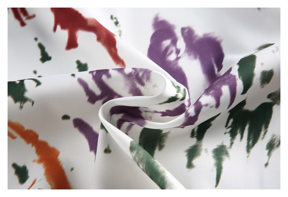 Close-up of the cream fabric draped in folds, showing an abstract print in purple, green, orange, and red.