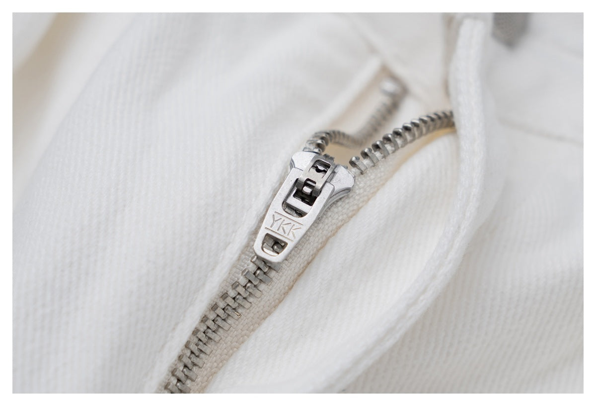 Close-up of a metal zipper and pull on white jeans.
