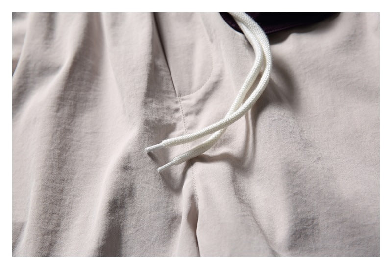 Close-up of white drawcord ends and pocket stitching on light beige shorts.