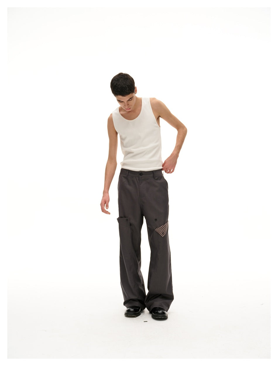 Model looking down in a cream tank top and charcoal wide-leg trousers with a plaid accent on one front pocket.