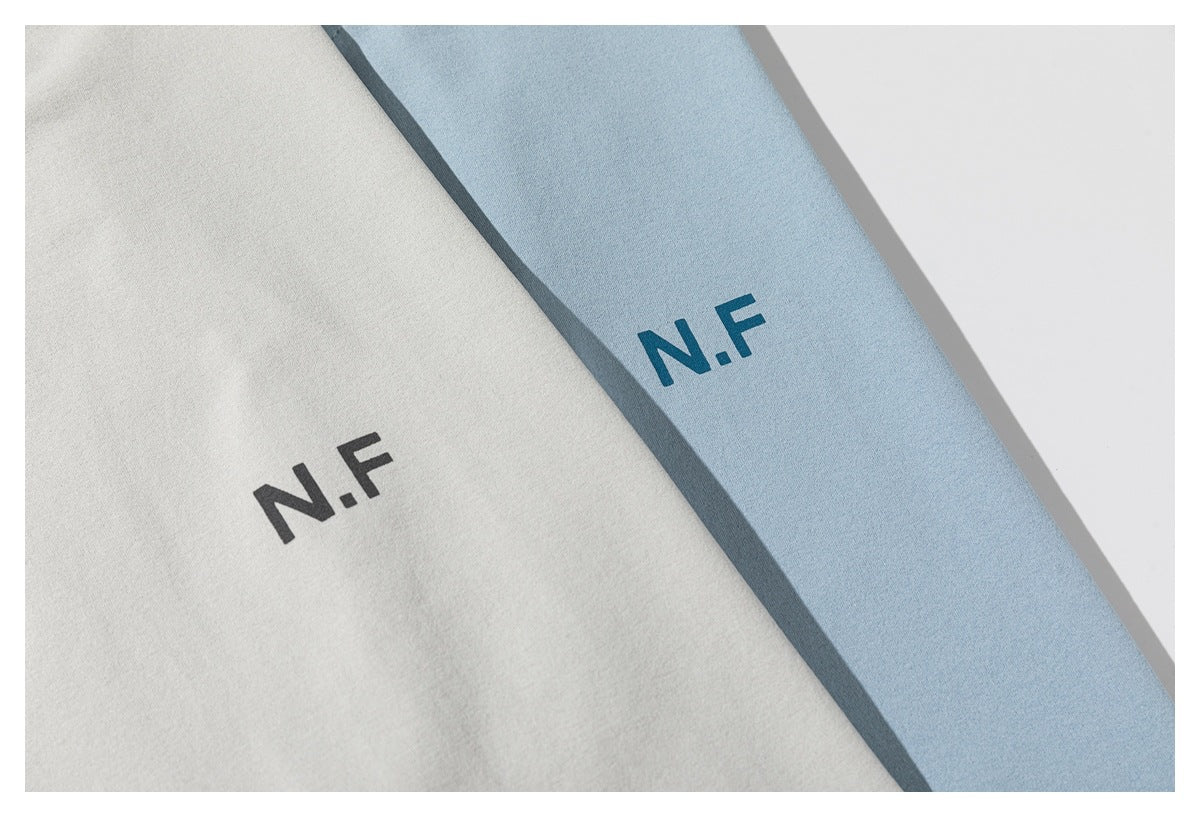 Close-up of light gray and light blue T-shirts showing the N.F chest print in black and teal.