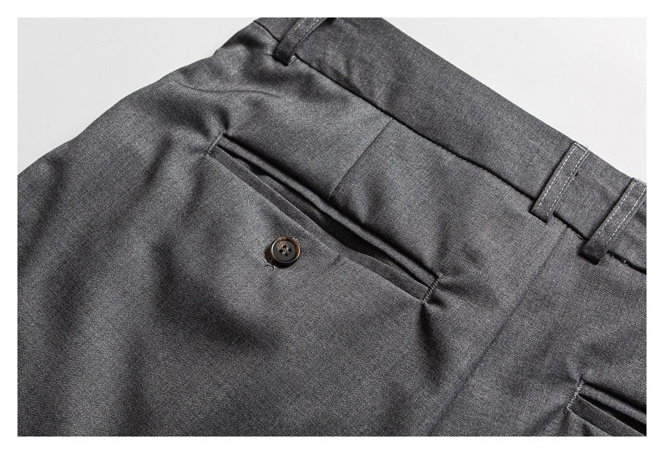 Close-up of gray trousers showing a buttoned welt pocket, waistband, and belt loops.