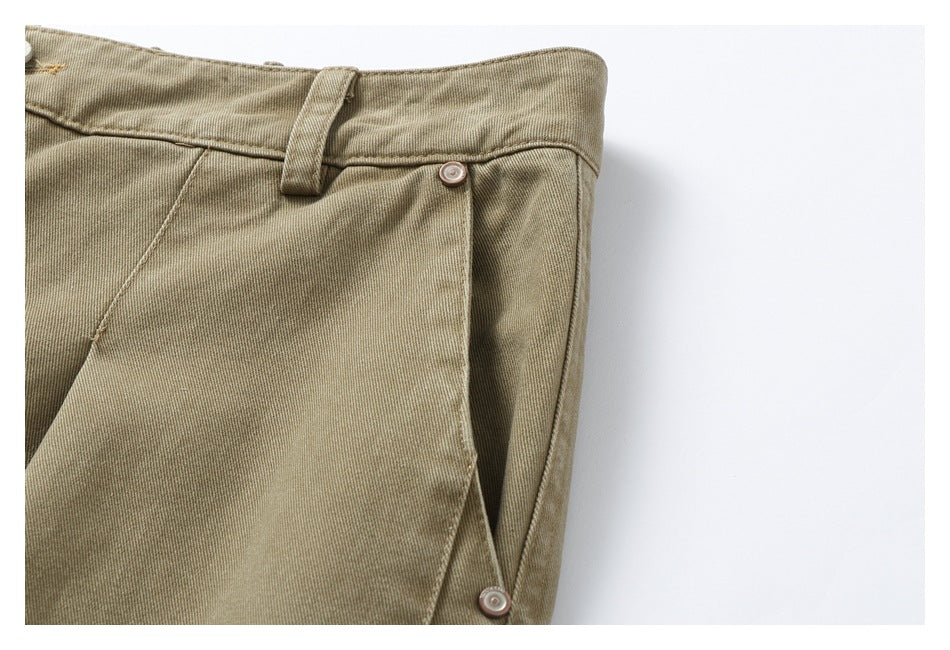 Close-up of tan pants showing a belt loop, side pocket seam and two round metal buttons.