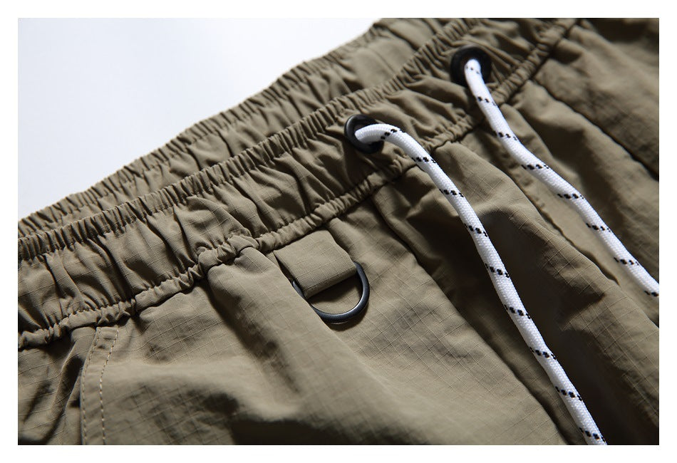 Detail of the olive-khaki shorts' elastic waistband, white patterned drawstrings, and black D-ring tab.