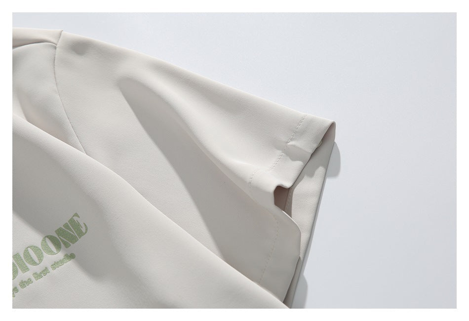 Close-up of the ivory shirt's short sleeve and stitched cuff, with part of the green chest print visible.