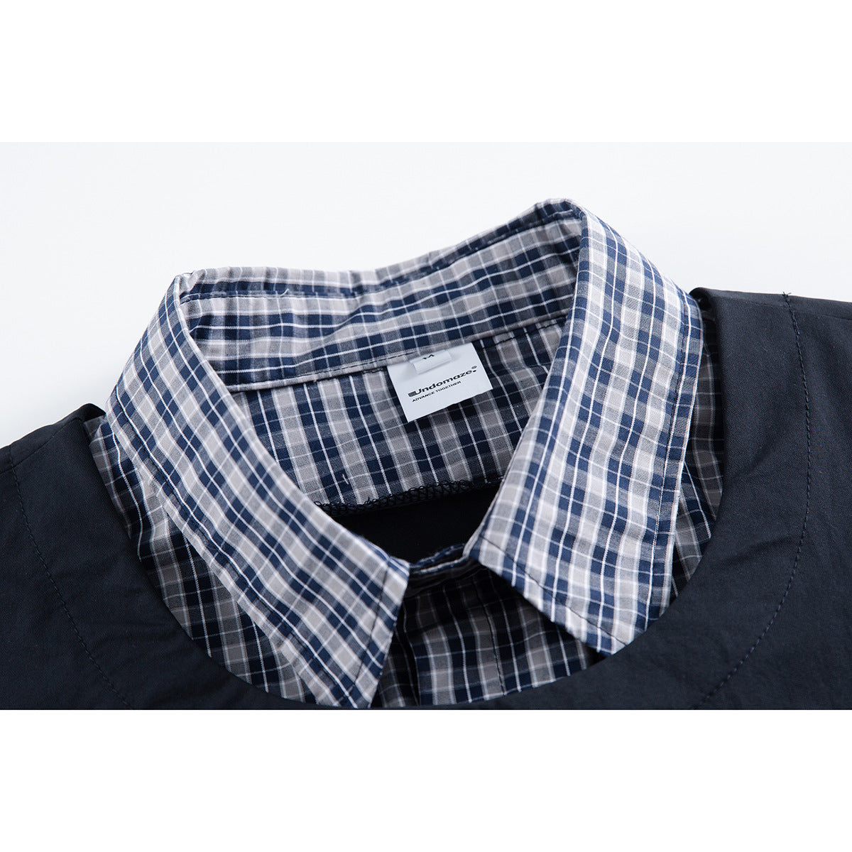 Close-up of a navy, gray, and white plaid shirt collar with a small sewn-in label.
