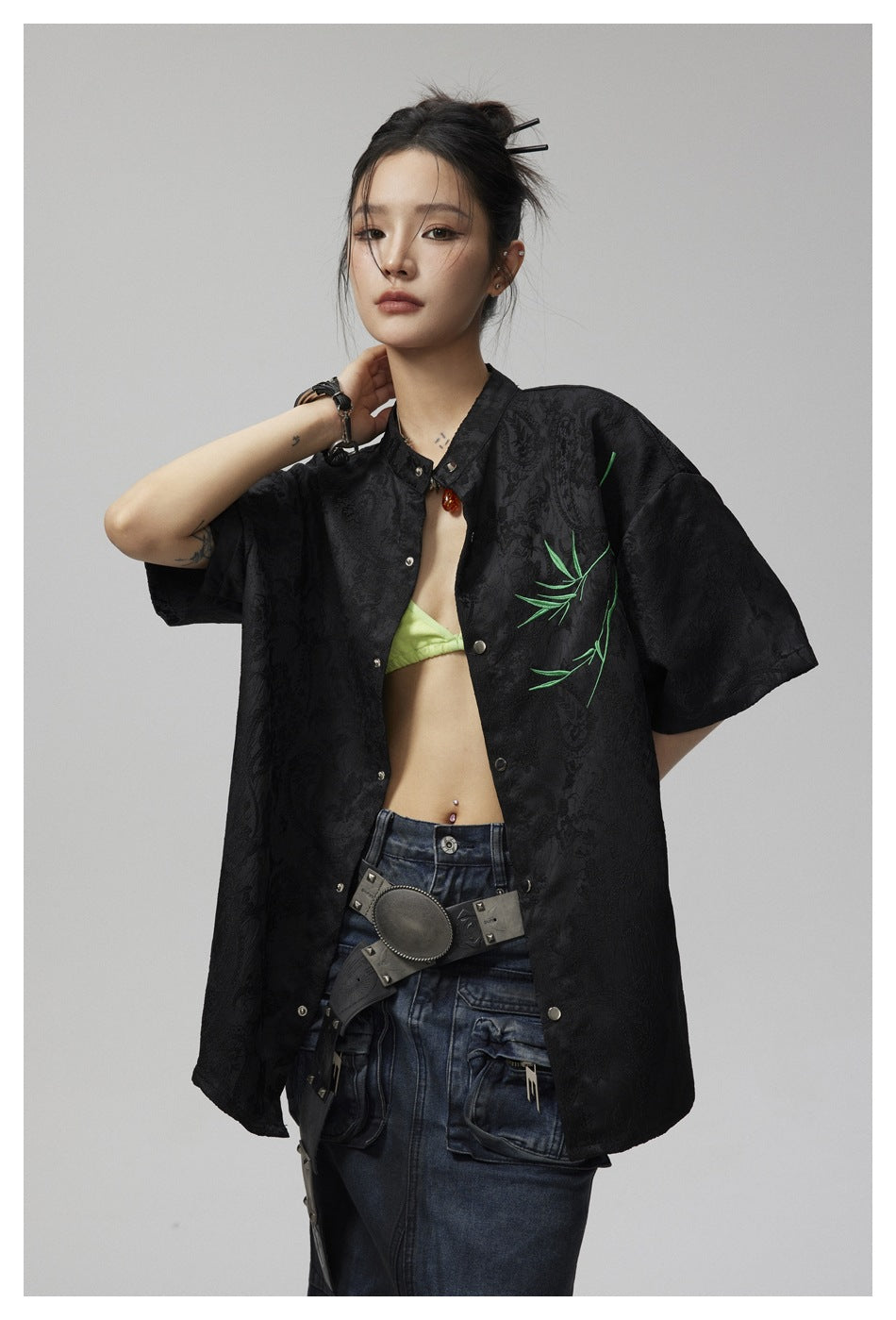 Close view of an oversized black patterned button-up shirt with green branch embroidery, worn by a model.