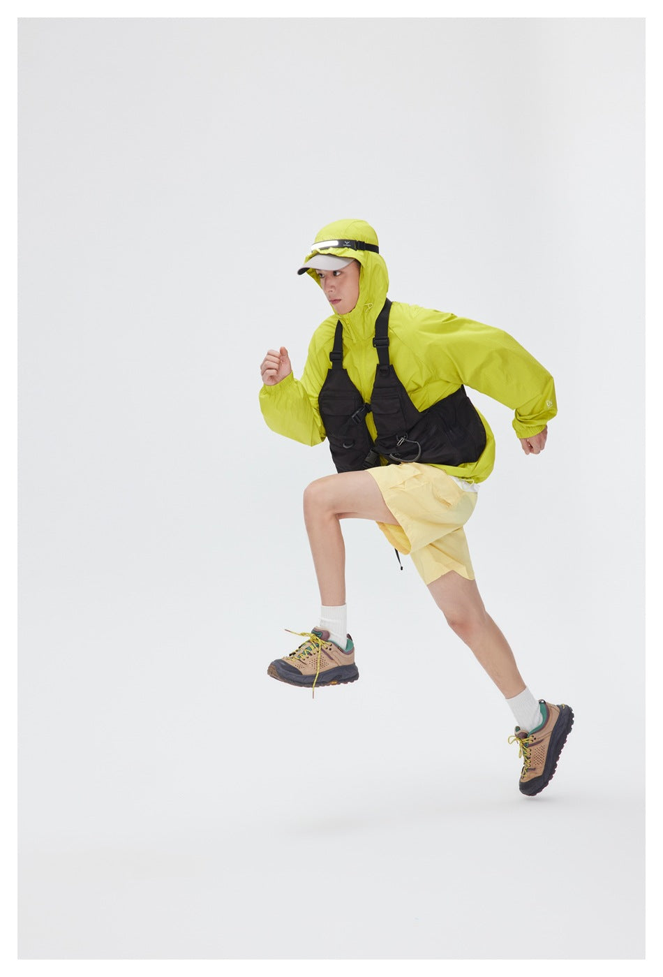 Model running in a bright lime-green hooded jacket, yellow shorts and a black chest bag.