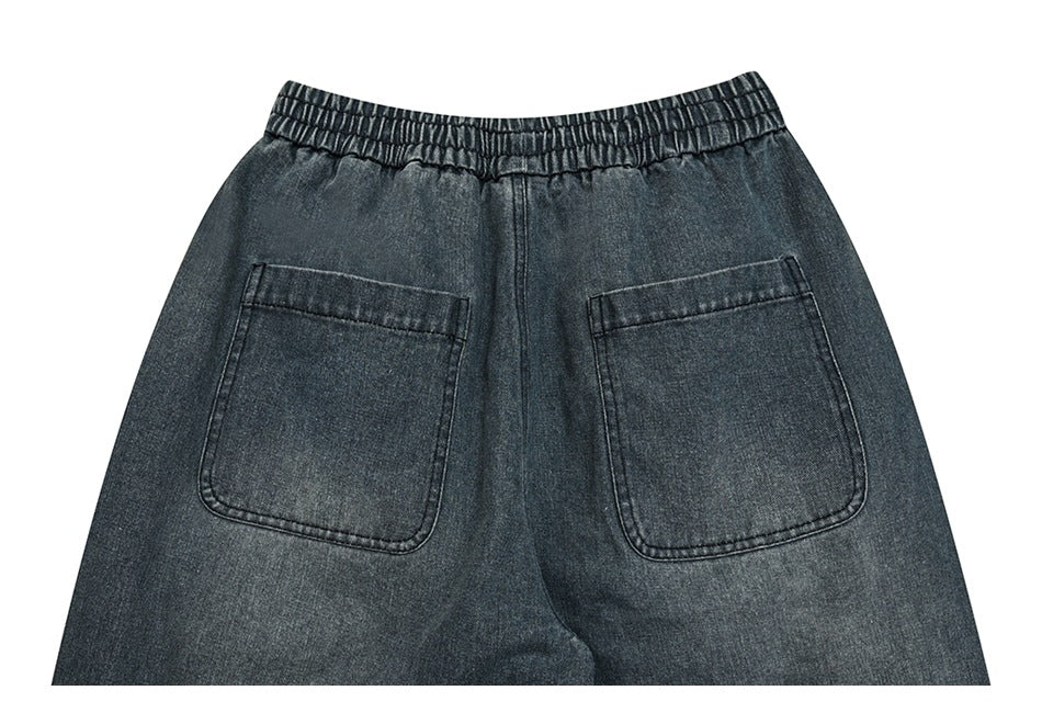 Back view of dark charcoal denim trousers with an elastic waistband and two large patch pockets.