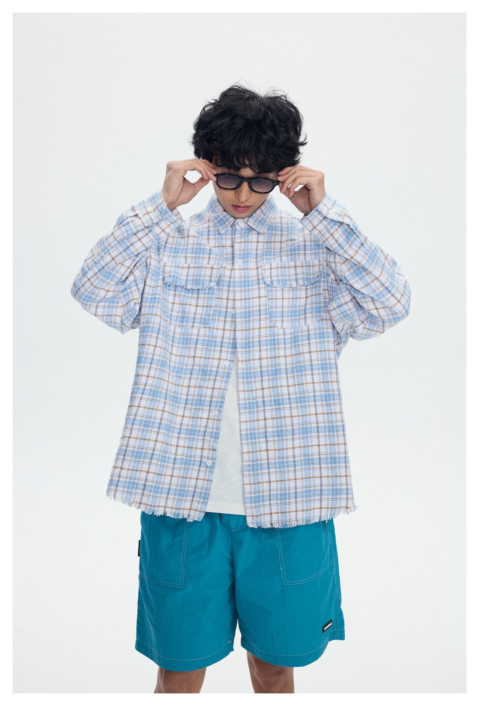 Model wearing a pale blue and tan plaid button-up shirt with frayed hems and teal shorts.
