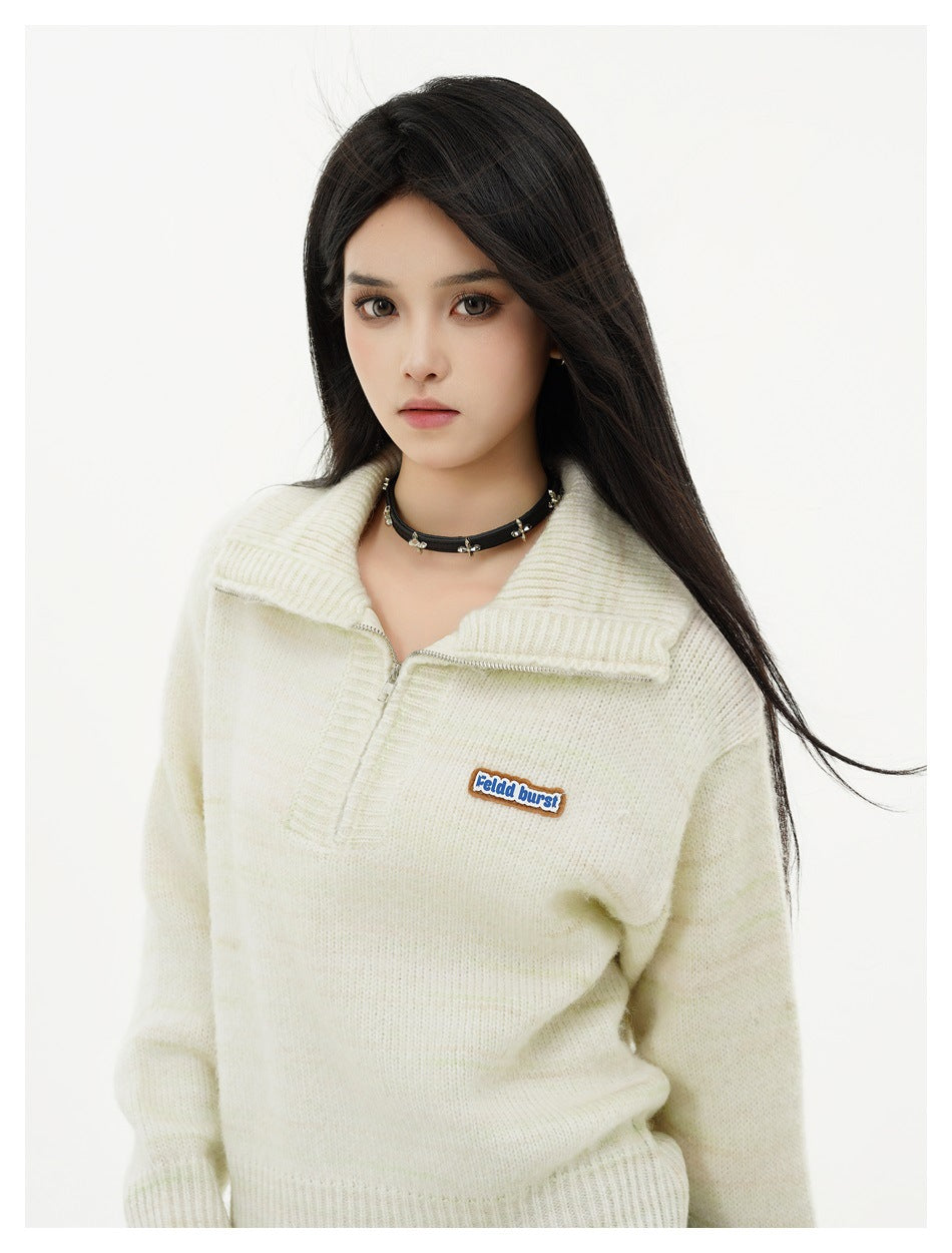 Close view of a model wearing an ivory knit pullover with a wide collar, short zipper, and small chest patch.