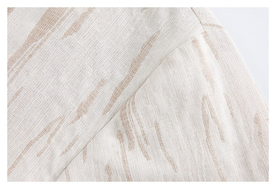 Close-up of cream fabric with tan abstract streaks and a diagonal folded seam.