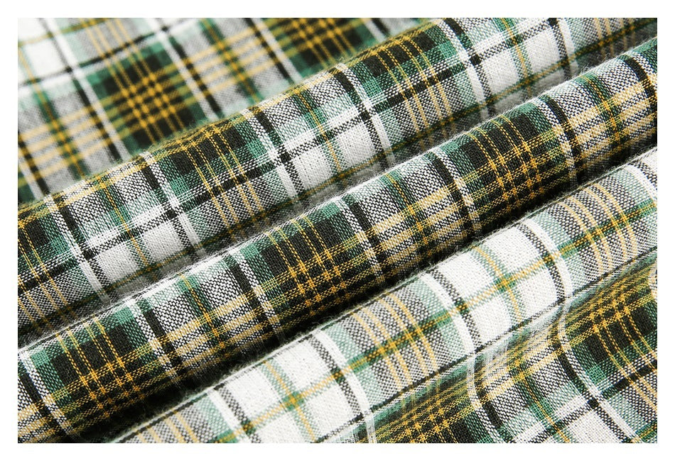 Macro view of the white, green, black, and mustard plaid shirt fabric arranged in soft folds.