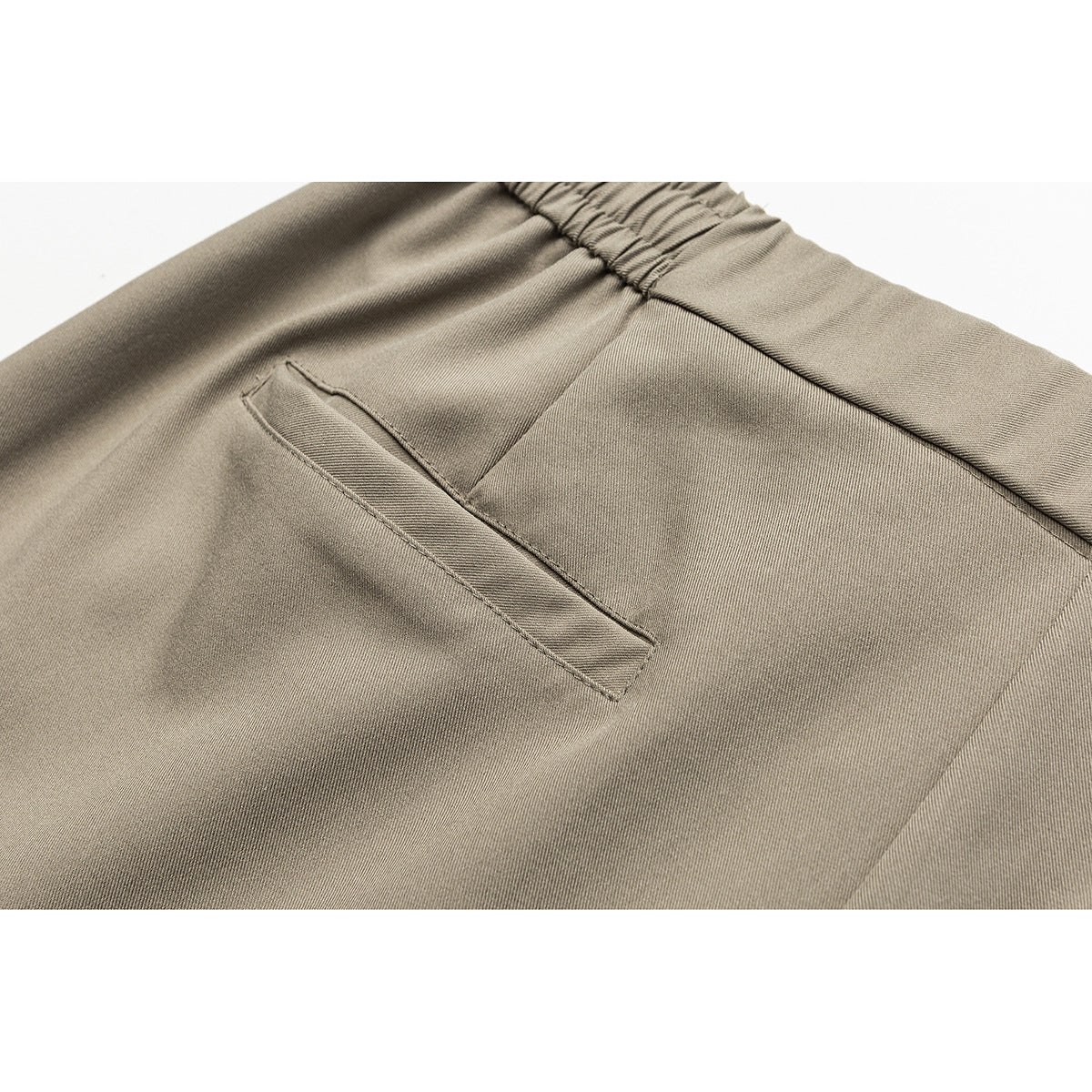 Close-up of taupe trousers showing the gathered back waistband and a single welt pocket.