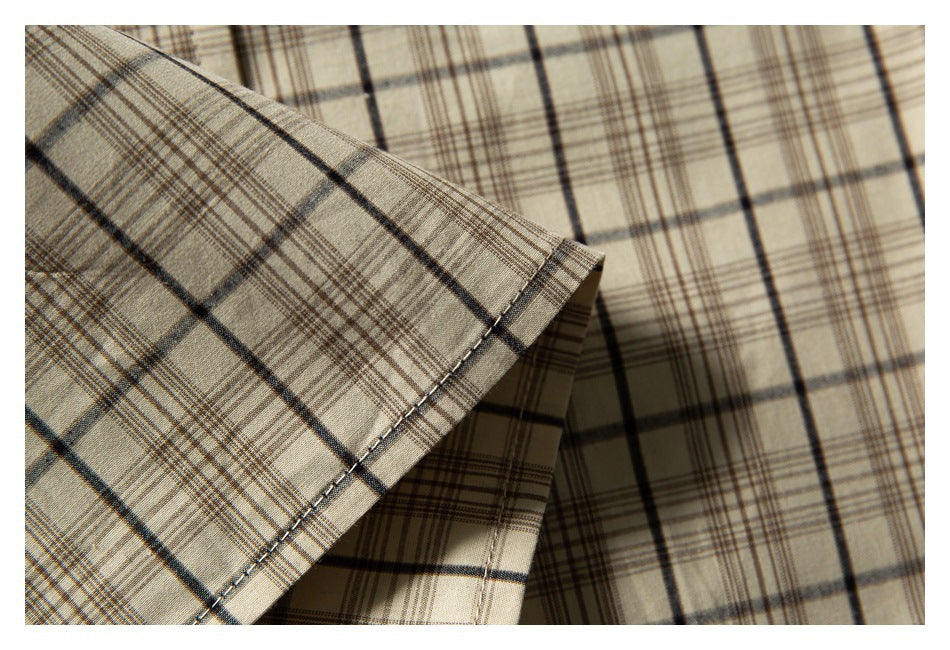 Close-up of a stitched sleeve hem on a beige shirt with dark plaid lines.