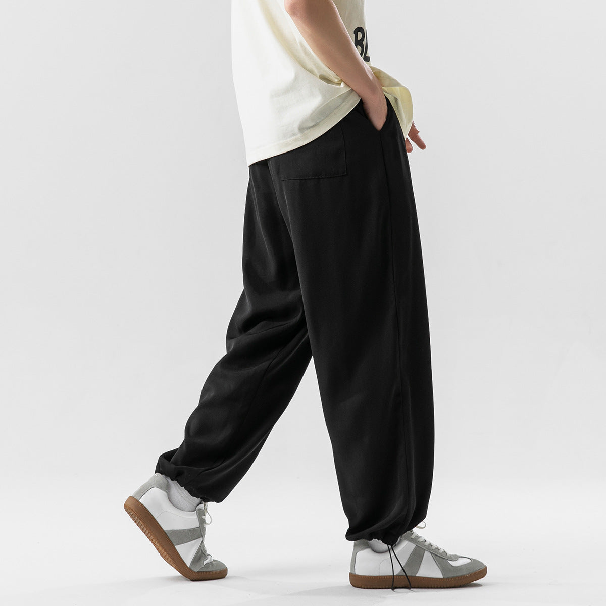 Side view of a person wearing loose black trousers with a rear patch pocket and gathered ankle cuffs.