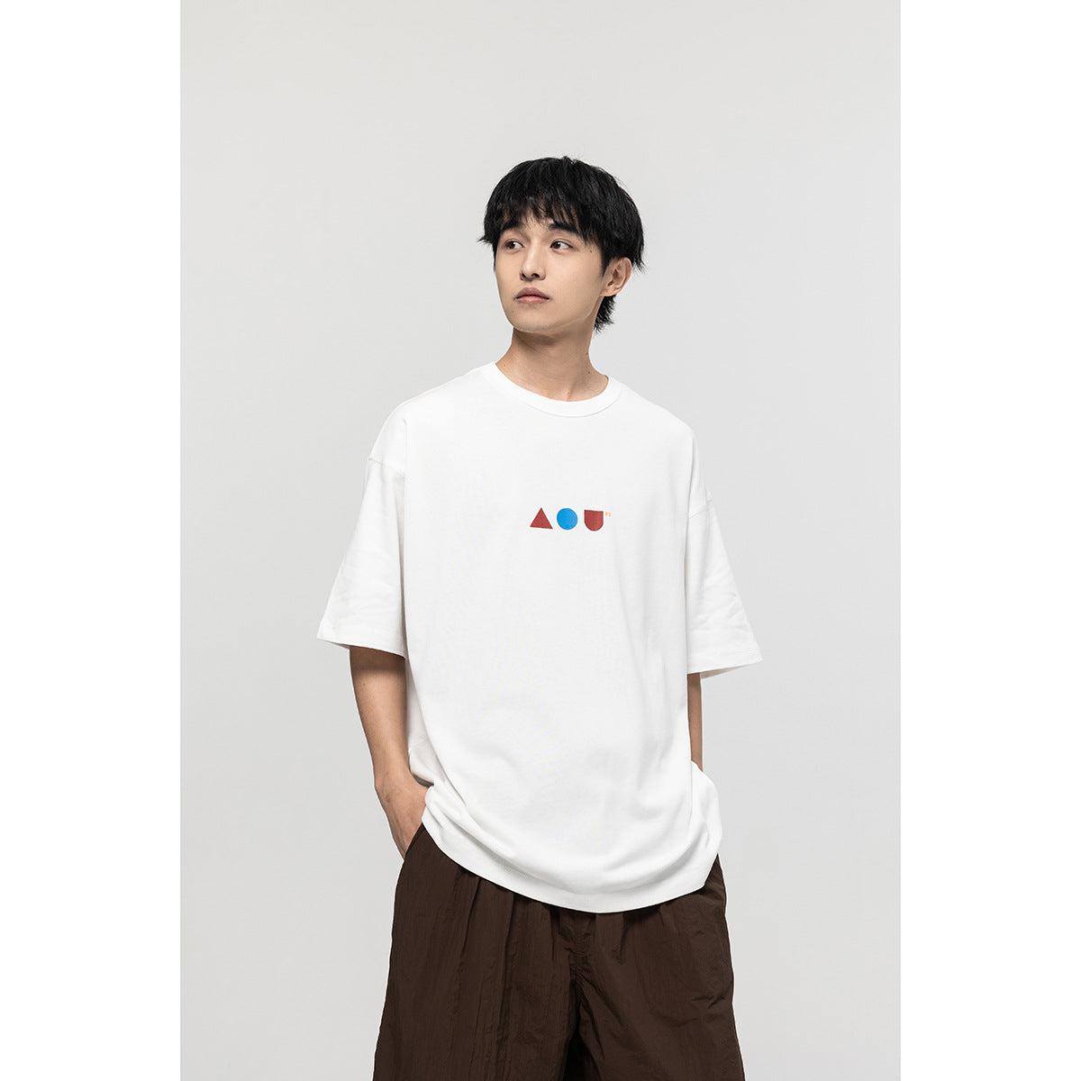 Model wearing a white oversized T-shirt with small red and blue geometric chest graphics.