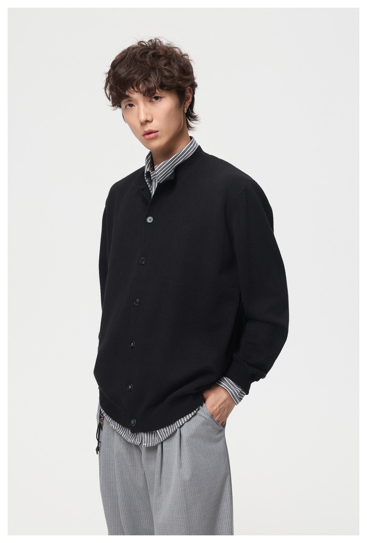Model wearing a black button-front cardigan over a striped shirt, in a three-quarter view.