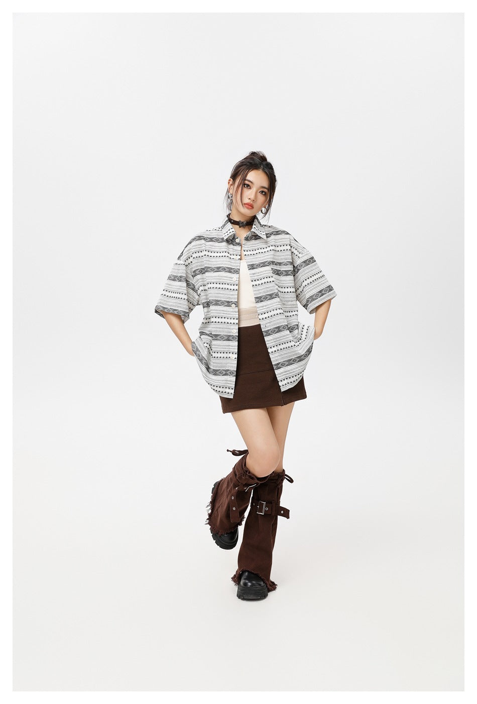 Model wearing an open oversized white shirt with black geometric stripes over a light top and brown mini skirt.