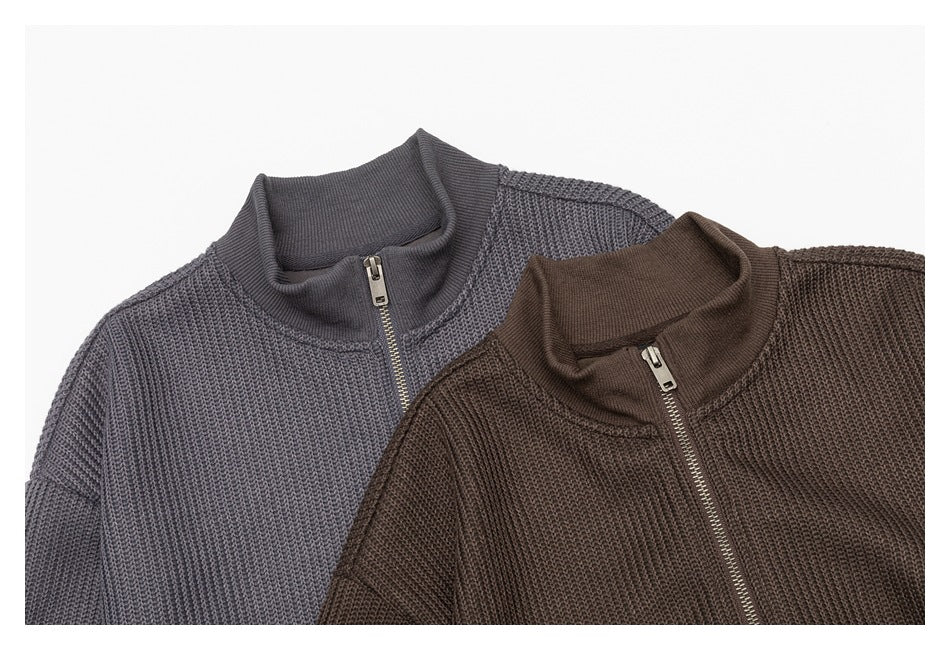 Close-up of two chunky knit zip-up sweaters in charcoal gray and dark brown, showing their stand collars and metal zippers.