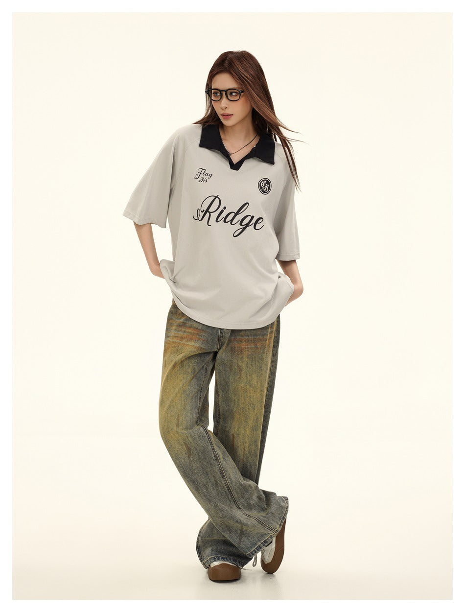 Model wearing gray short-sleeve polo-style T-shirt with black collar, glasses and faded wide-leg jeans, full-length view