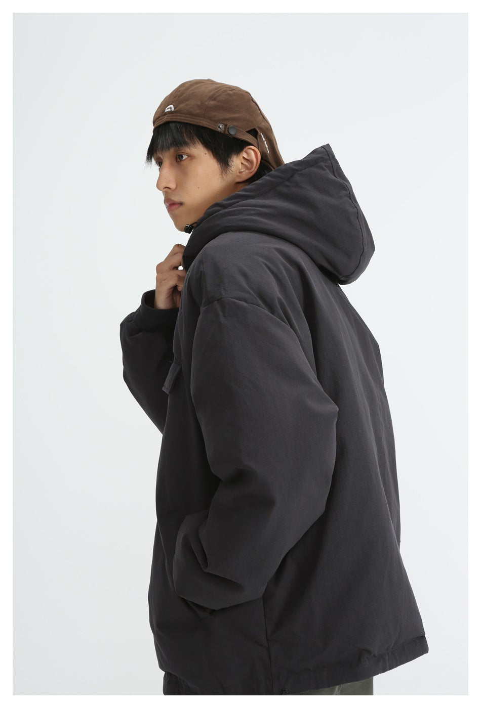Side view of model in black hooded padded jacket with dropped shoulder and brown cap