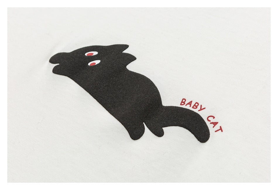 Close-up of a black cat graphic with red eyes and the words “BABY CAT” on ivory fabric.