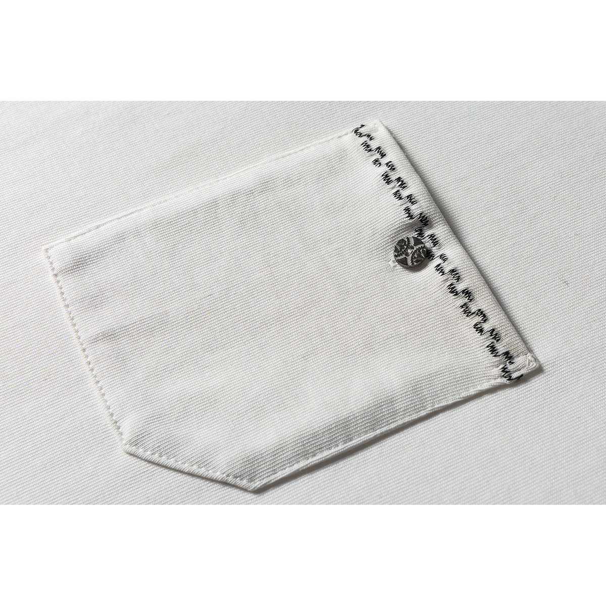 Close-up of a white shirt pocket with a metallic button and black decorative stitching along the edge.