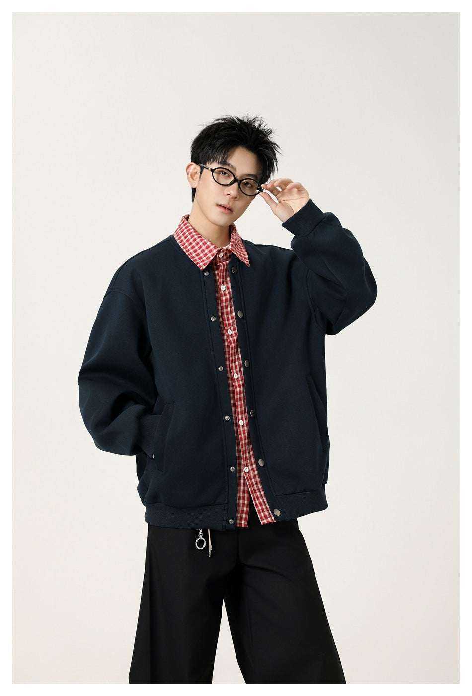 Model wearing a dark navy snap-front jacket over a red checked shirt and black trousers.