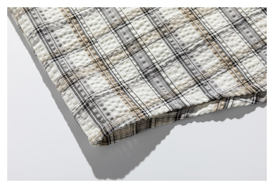 Close-up of the hem of a cream, black, and tan plaid shirt laid flat.
