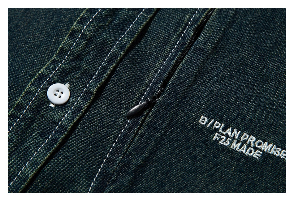 Close-up of the dark blue-green shirt placket with a white button, black zipper pull, and white chest embroidery.