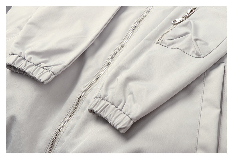 Close-up of a light gray jacket showing its front zipper, zip pocket, sleeves, and elastic cuffs.