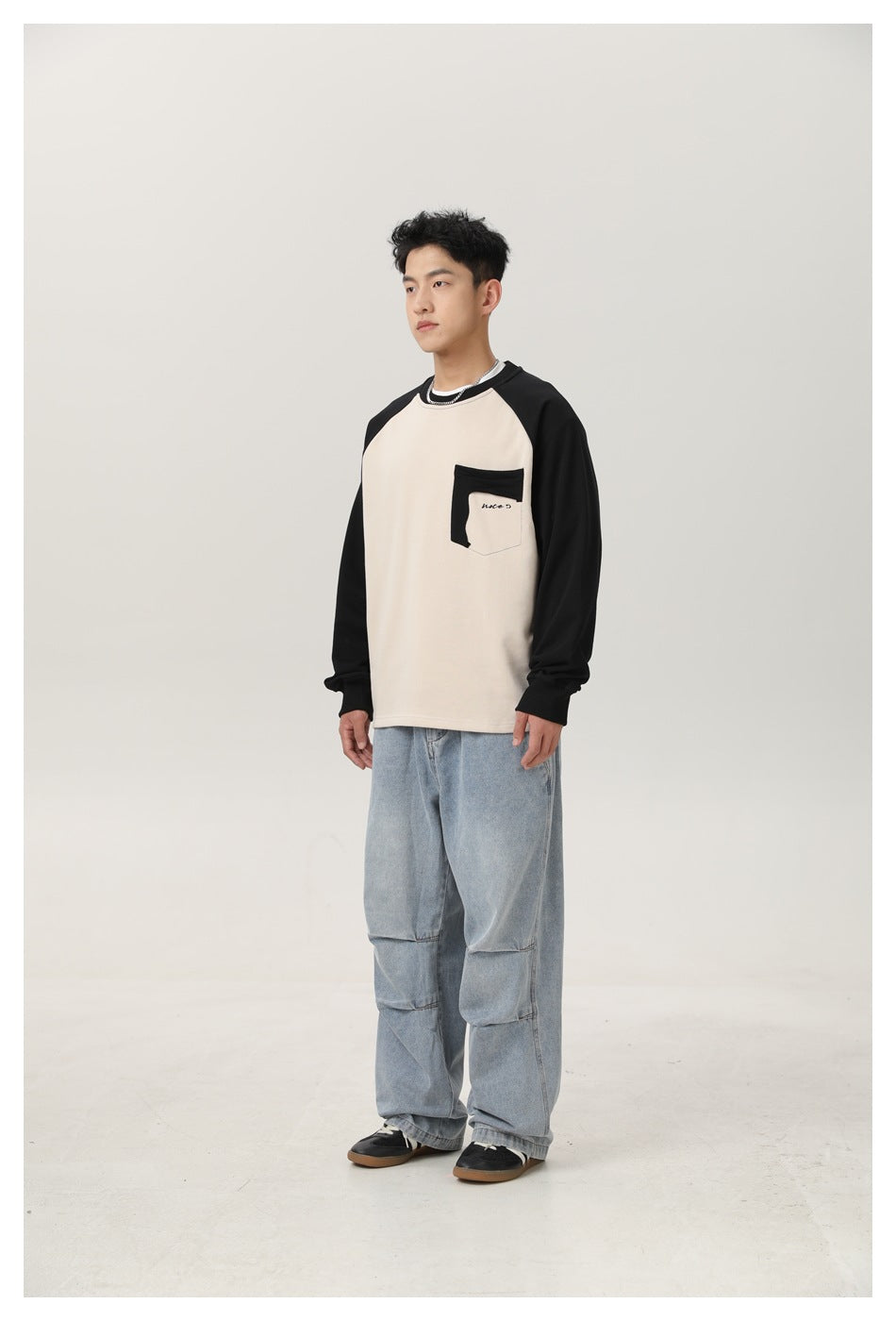 Model in a beige and black raglan sweatshirt with light-wash jeans, angled three-quarter view
