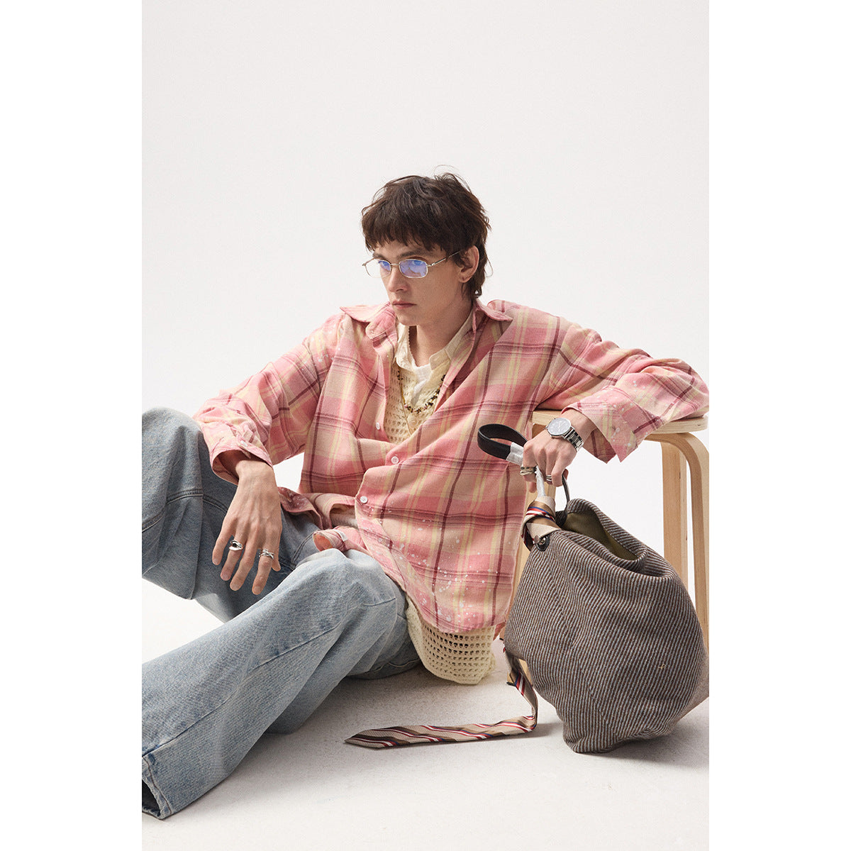 Model seated in a pink plaid button-up shirt with white splatter details, layered over a cream knit top.