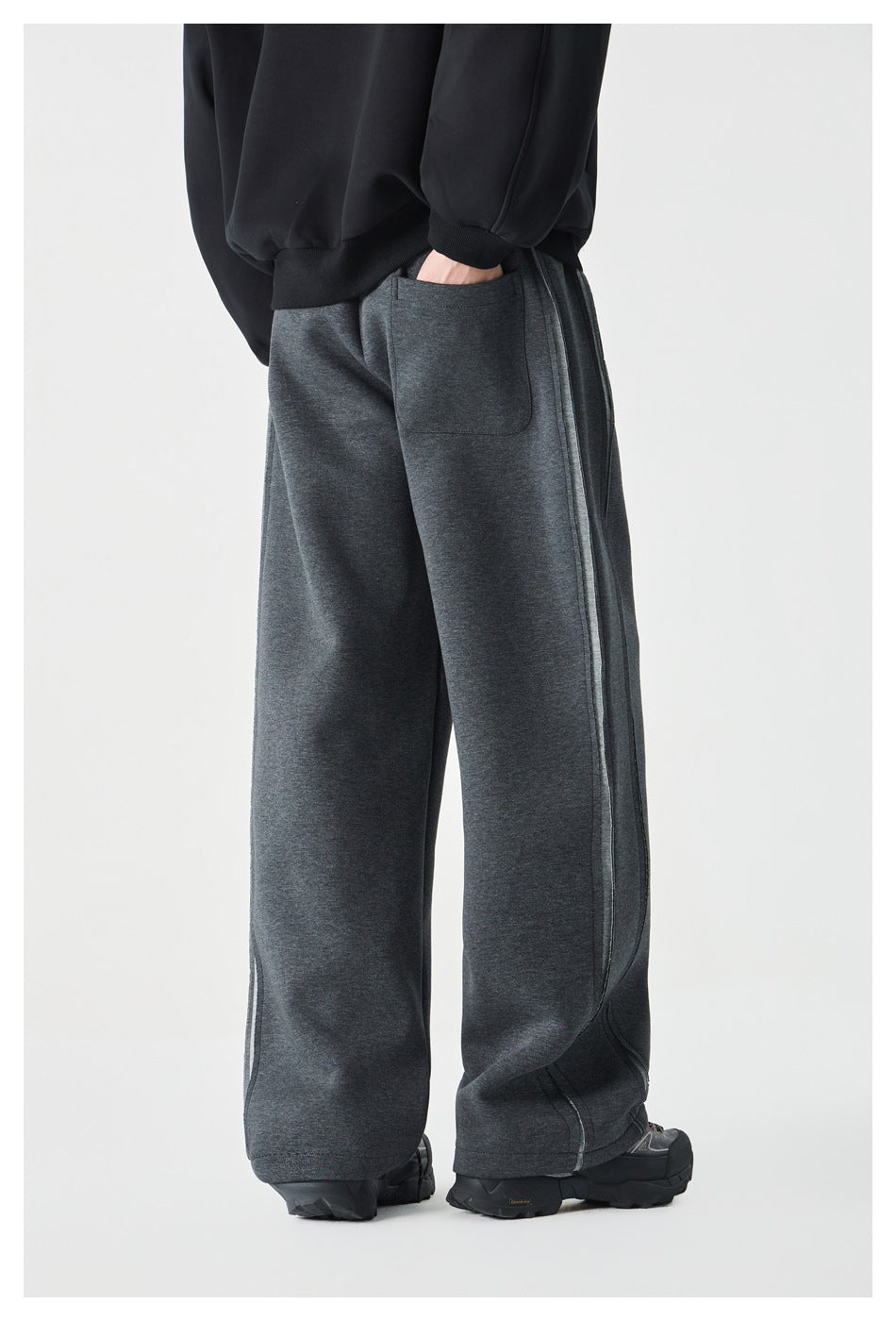 Rear three-quarter view of a model wearing charcoal wide-leg sweatpants with a back pocket and seam detailing.