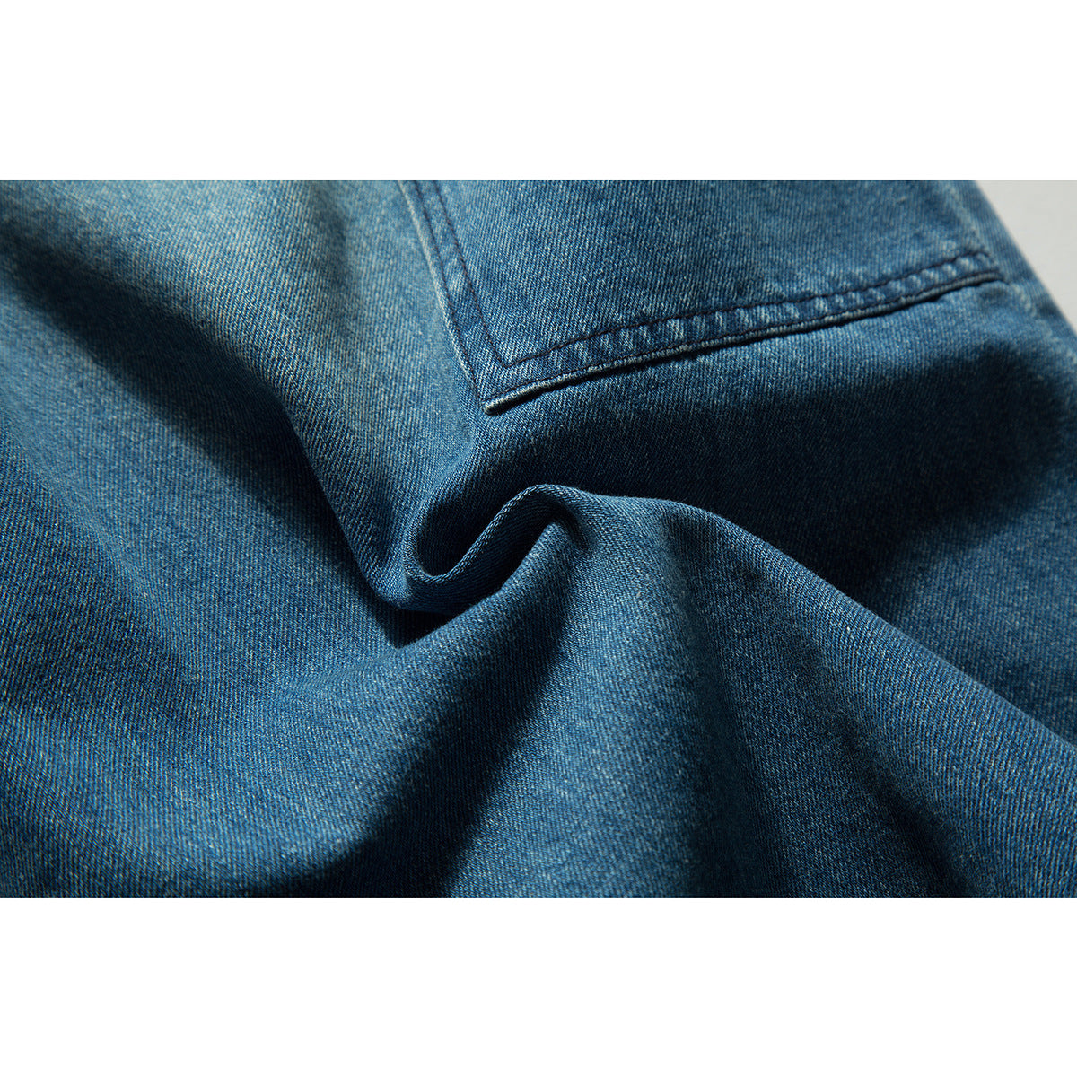 Close-up of blue denim shorts showing the fabric texture, folds and a stitched pocket edge.