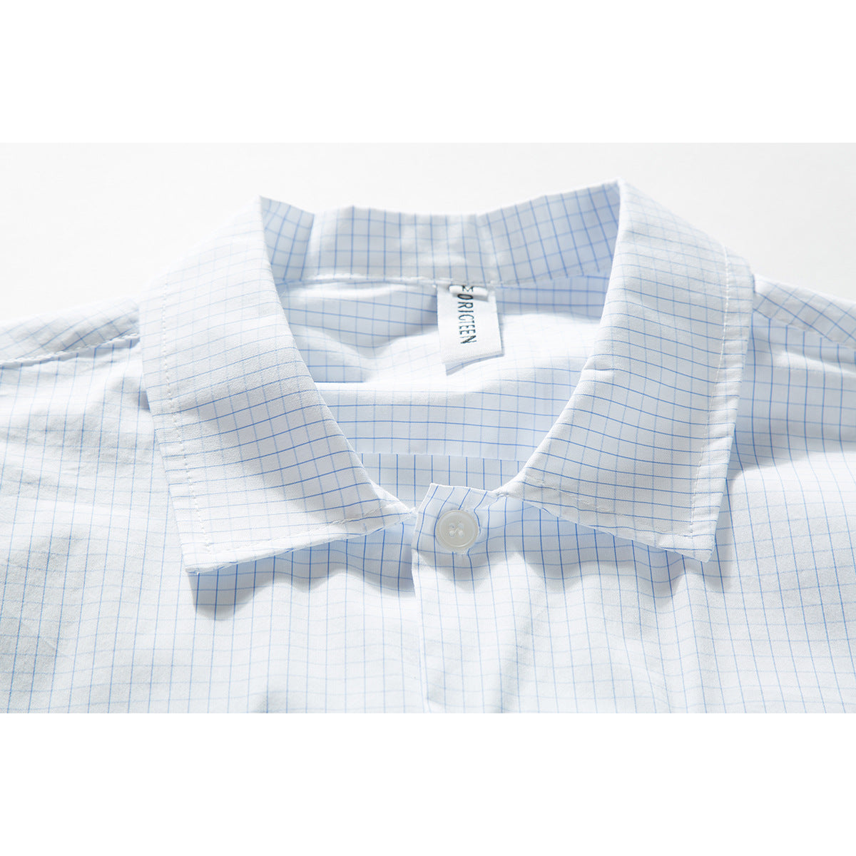 Close-up of a white shirt with a light blue grid pattern, showing its pointed collar and top button.