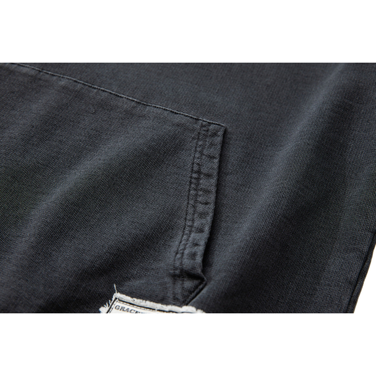 Close-up of a charcoal hoodie pocket seam and textured fabric, with part of a small garment label visible.