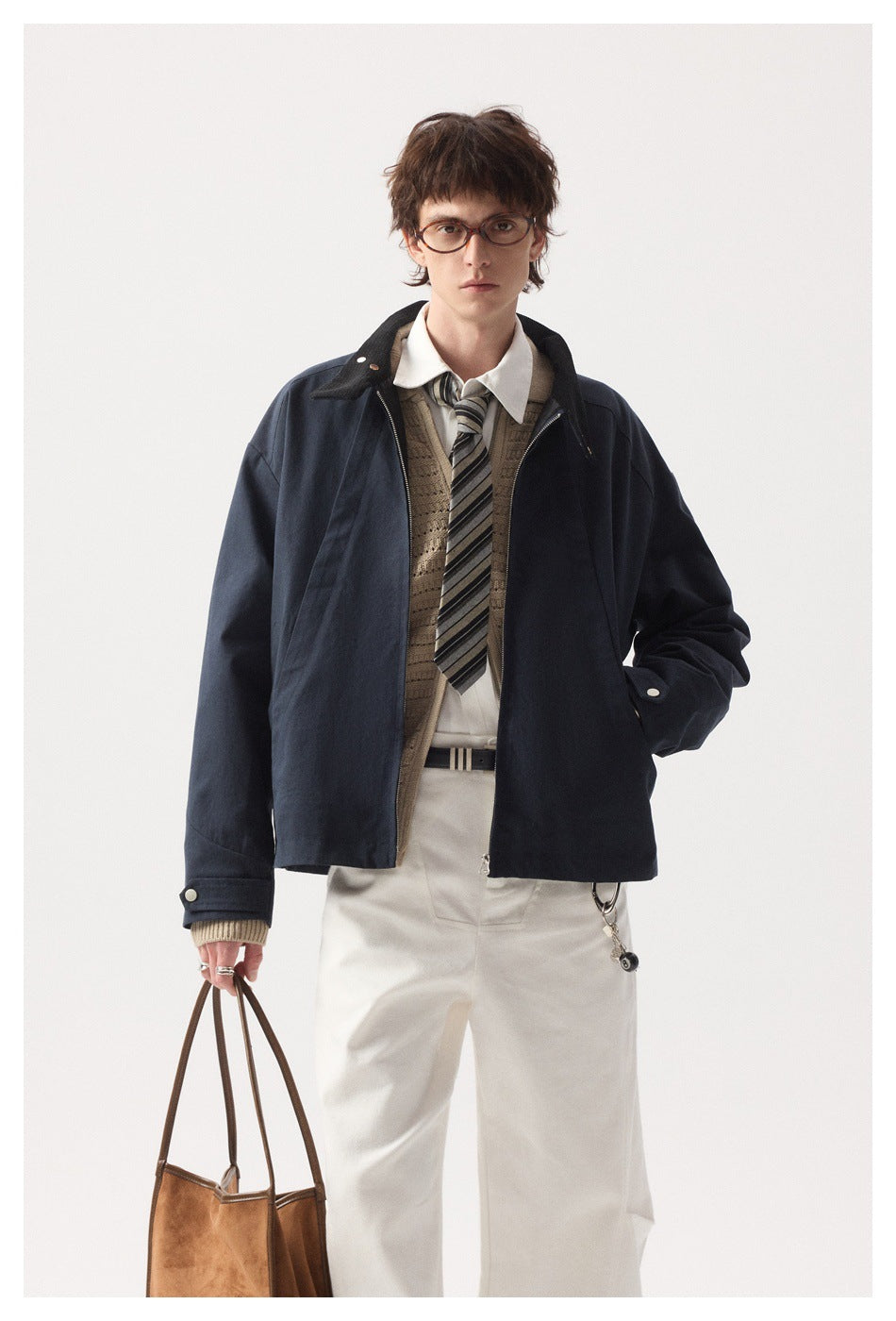 Model in a navy zip jacket with a dark collar, layered over a knit vest, shirt and striped tie.