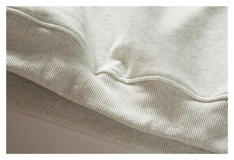 Close-up of the ribbed waistband and stitched hem of a light gray heathered sweatshirt.