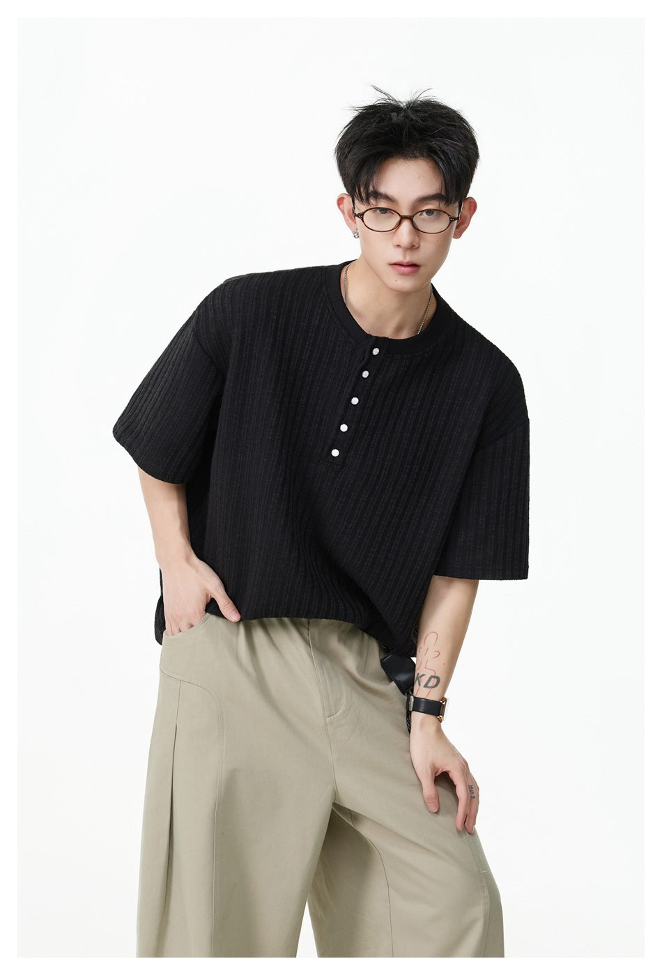 Model wearing a black ribbed short-sleeve Henley T-shirt with snap buttons and wide khaki trousers