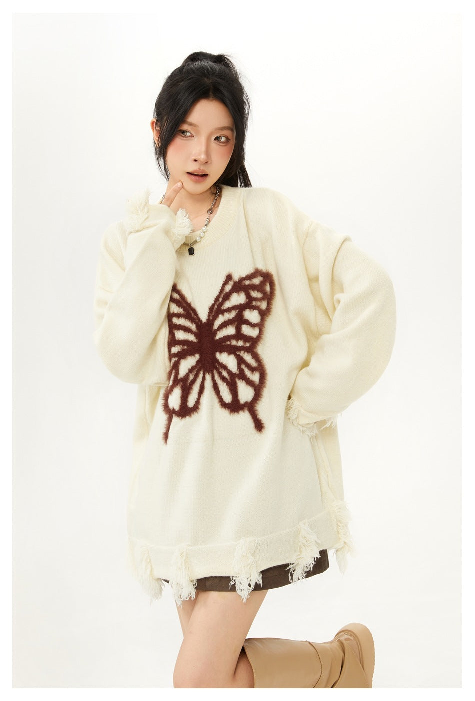 Closer view of a model wearing an ivory sweater with a large brown butterfly motif and frayed trim.