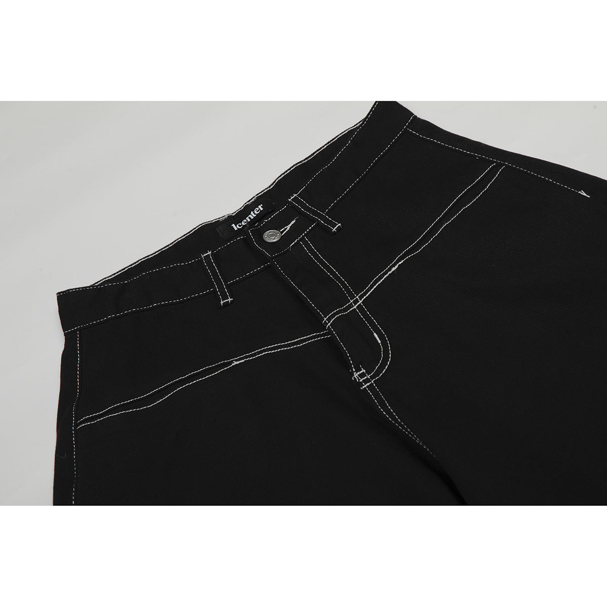 Close-up of black trousers showing the waistband, button fly, front pocket and contrasting white stitching.