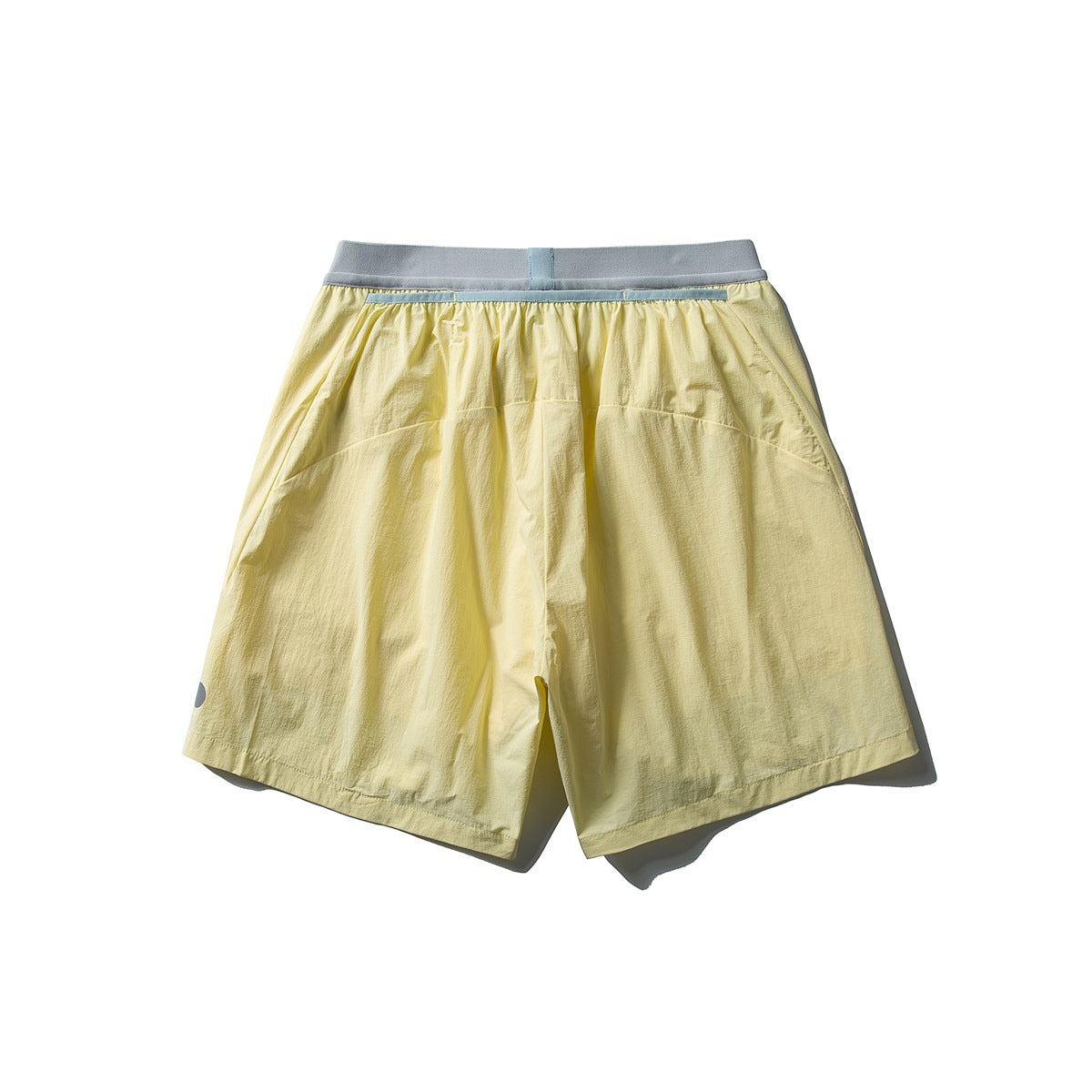 Back view of loose pale yellow shorts with a gray-blue waistband and curved rear panel seams.