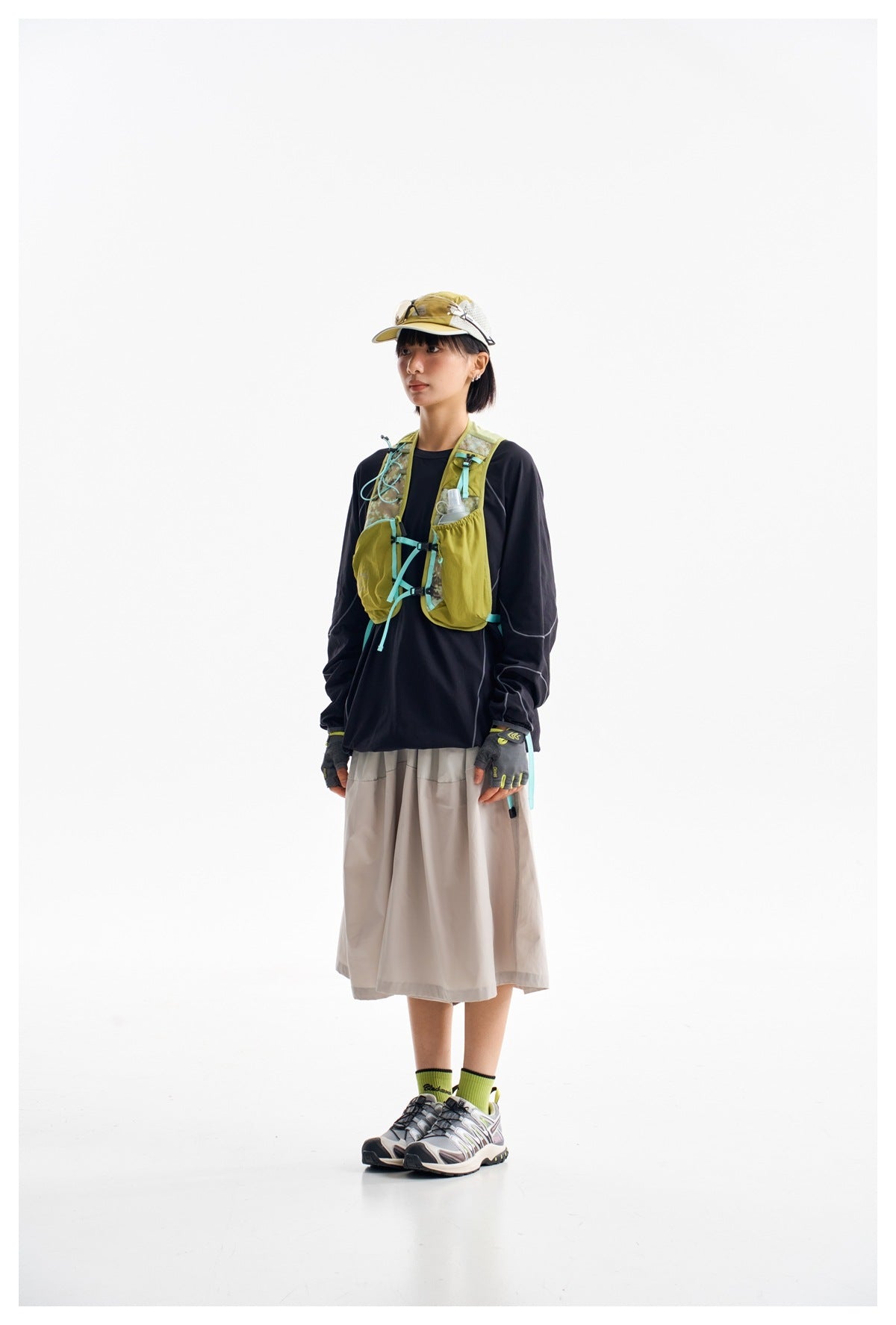 Full-length model wearing a lime-green running vest with turquoise details over a black top and light skirt.