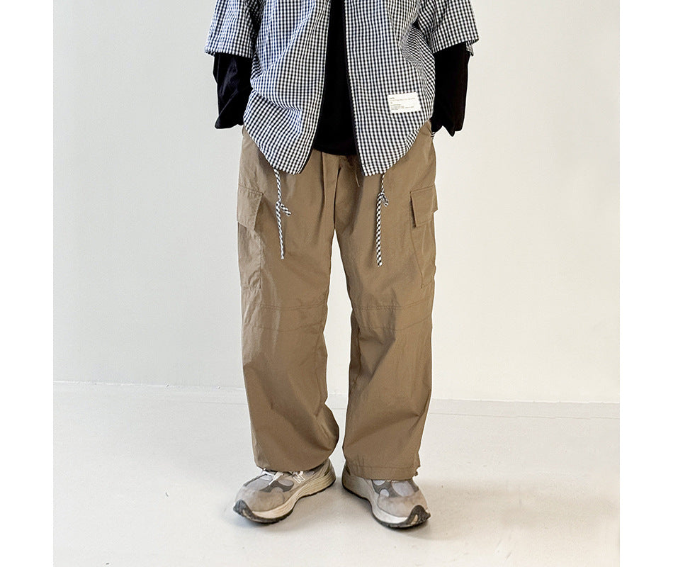 Person wearing khaki wide-leg cargo pants with a gingham short-sleeve shirt over a dark layer and gray sneakers
