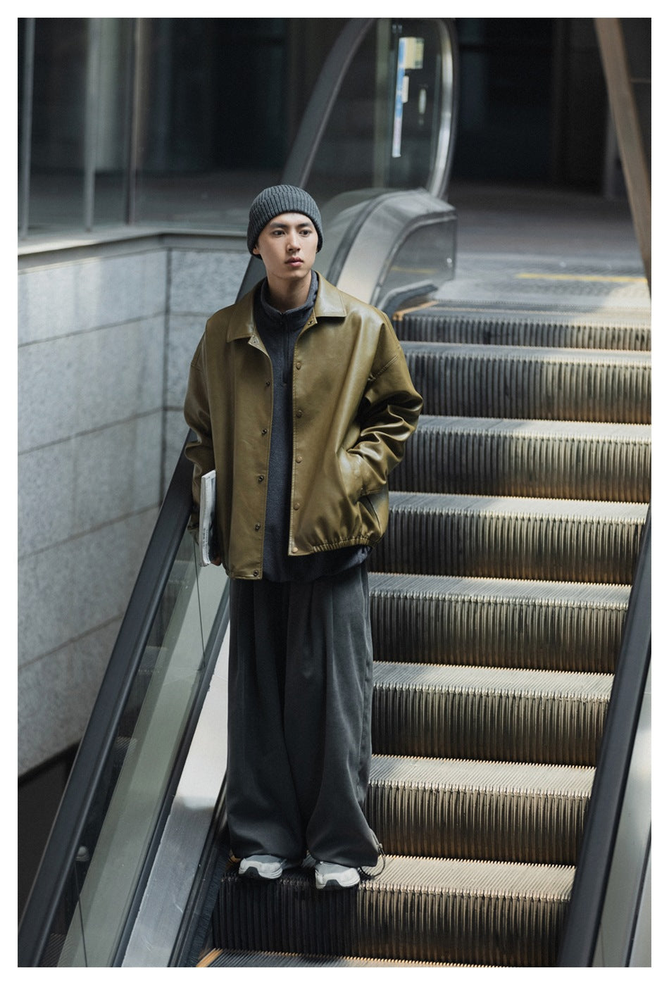 Full-length front view of a man wearing an olive button-front jacket, gray beanie, dark trousers, and sneakers.