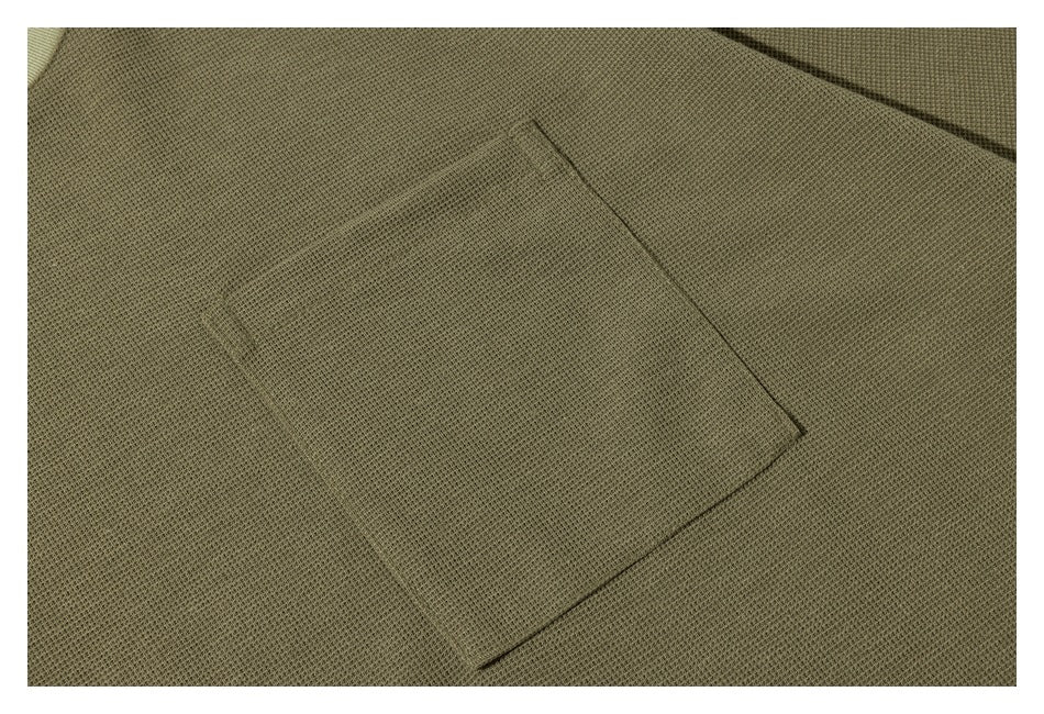 Close-up of a square chest pocket on olive-green textured knit fabric.