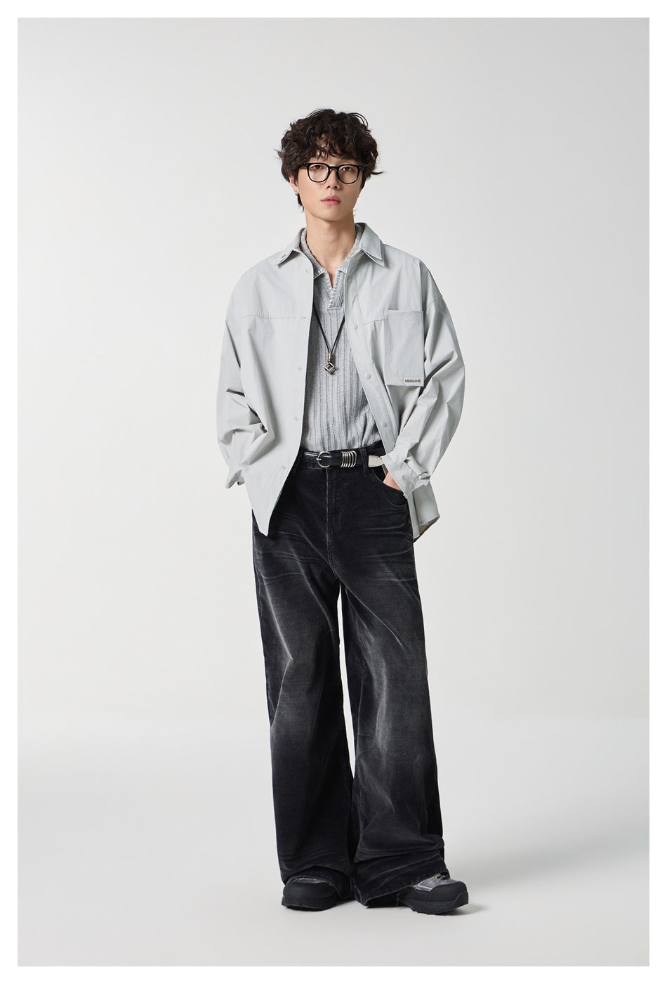 Model wearing a light gray oversized button-front shirt over a gray knit top, with wide black trousers.