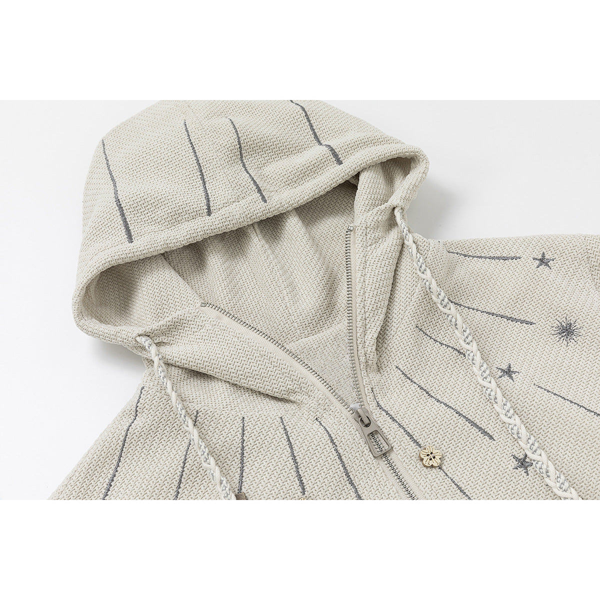 Close-up of an ivory textured hoodie with a zip front, braided drawstrings, and gray shooting-star motifs.